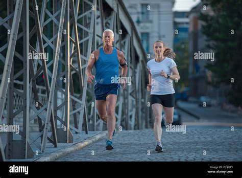 Healthy Mature Couple Jogging In The City At Early Morning With Sunrise In Background Stock