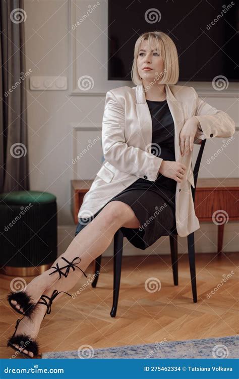 Portrait Of Middle Aged Woman Sitting On Chair With Crossed Legs At
