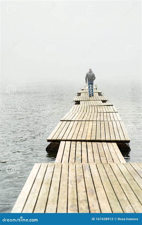 Lonely Guy Walking Along A Long Wooden Bridge On A Lake Stretching Into