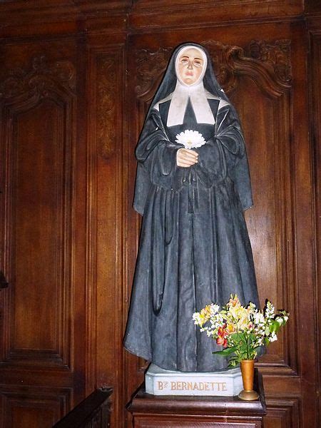 A Statue Of A Nun Holding A Flower In Front Of A Wooden Paneled Wall