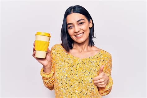Jovem e bela mulher latina segurando uma xícara de café para viagem sorrindo feliz e positiva