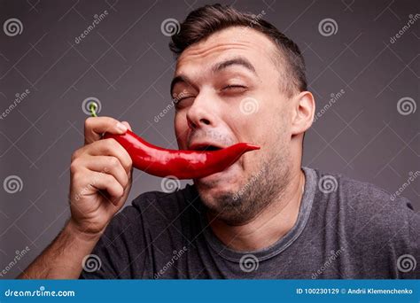 Funny Guy Eating Red Chili Pepper On A Gray Background Handsome Man With Spicy Hot Pepper