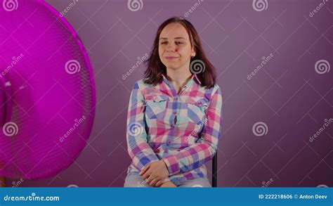 Acercamiento De Una Joven Sentada En Una Silla Frente A Un Ventilador Con Fondo Morado Brunette