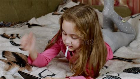 A Cute Blonde Haired Girl Lies On The Sofa Her Legs Dangling Carefully Looks At The Smartphone