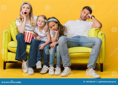 Parents And Kids Watching Movie On Sofa With Popcorn Bucket On Yellow