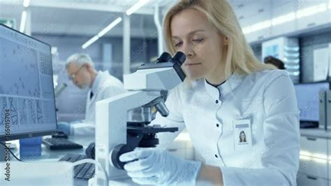 Female Research Scientist Looks At Biological Samples Under Microscope