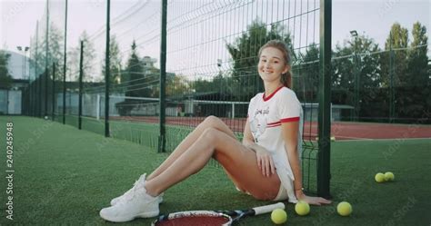 A Blonde Cute Lady On The Tennis Court Wearing A Beautiful Tennis Suit And Playing With A