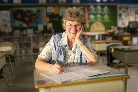 Happy Mature Female Teacher Sitting At School Desk Caucasian