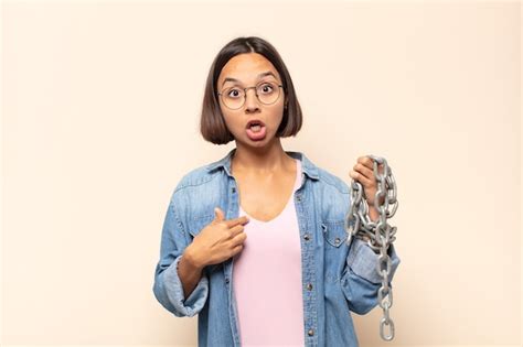 Joven mujer latina mirando consternado y sorprendido con la boca abierta apuntando a sí mismo