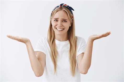 Perplexe Jeune Fille Blonde Posant Contre Le Mur Blanc Photo Gratuite