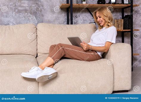Blonde Woman Sitting On Couch Using Tablet At Home In The Living Room Stock Image Image Of