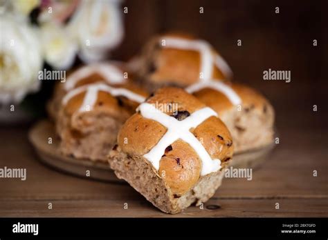 Hot Cross Buns With Flowers Behind Easter Treats On Old Board With