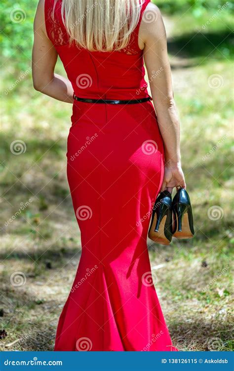 Beautiful Blonde Woman In Red Dress And Black Shoes In Hand Walks Through The Forest View From