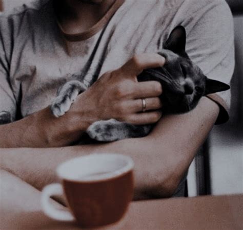 A Man Holding A Cat In His Arms Next To A Cup