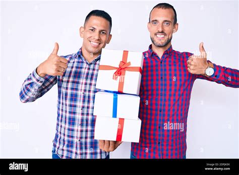 Jeune Gay Couple De Deux Hommes Tenant Cadeau Souriant Heureux Et Positif Pouce Vers Le Haut