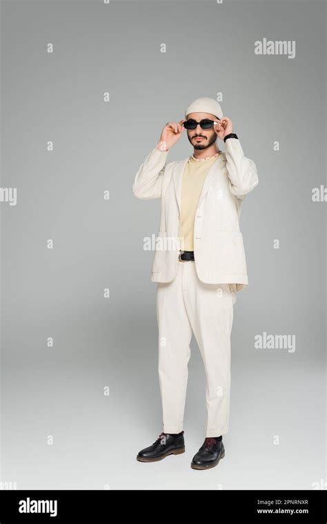 Full Length Of Trendy Gay Man In Beige Suit And Hat Wearing Sunglasses On Grey Background Stock