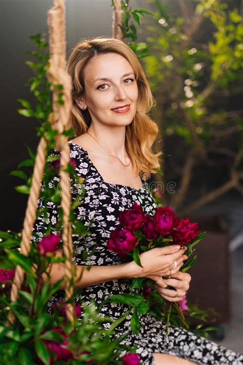 An Attractive Middle Aged Blonde Woman With Flowers Sits On A Swing Stock Photo Image Of