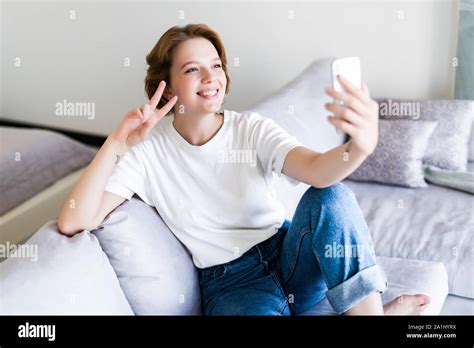Pretty Brunette Sitting On Her Sofa Taking A Picture Of Herself At Home In The Sitting Room