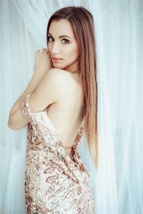 Beautiful Woman In Elegant Expensive Evening Shiny Gold Dress With Naked Rear With Dark Smokey