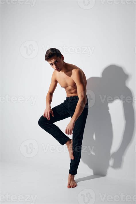 A Man With A Naked Torso Stands On His Leg Against A Light Background In Full Growth