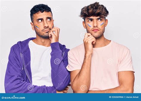 Joven Pareja Gay Dibujando La Bandera Lgtbq Arcoiris En La Cara Pensando Concentrado En La Duda