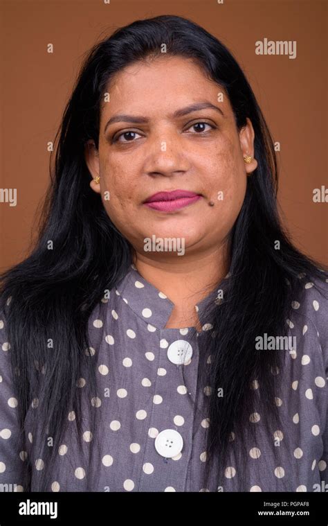 Portrait Of Mature Indian Woman Against Brown Background Stock Photo