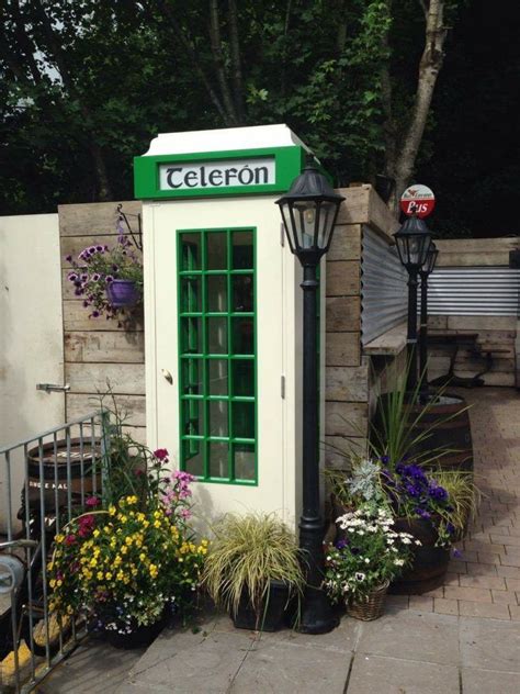 A Green Phone Booth Sitting On The Side Of A Road Next To Flowers And Trees