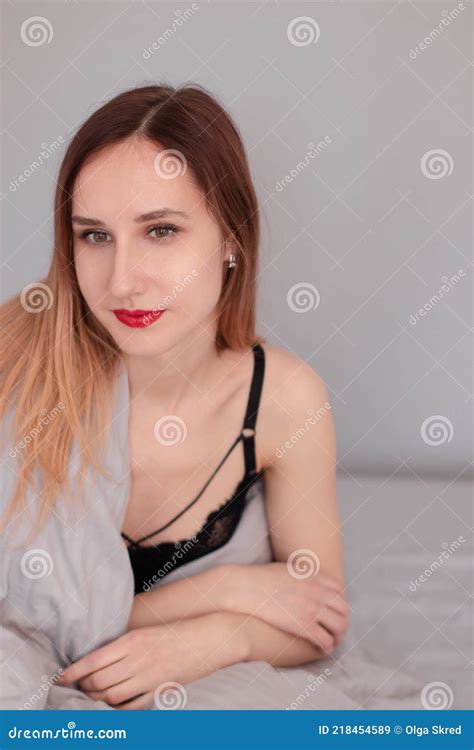 Portrait Of Pretty Redhead Woman In Black Lingerie On Bed With Grey Sheets And Blanket Stock