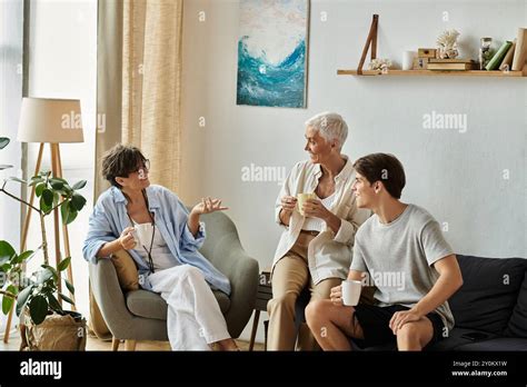 Lesbian Parents And Their Adult Son Share Laughter And Stories Over Warm Drinks In Their Sunny