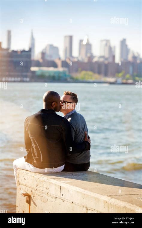 Vue arrière des hommes gay s embrasser tout en étant assis sur la rivière par un mur de