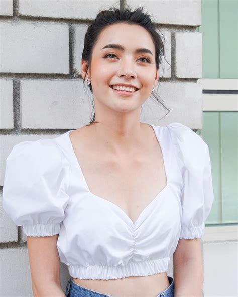 A Woman Standing In Front Of A Brick Wall Wearing A White Top With