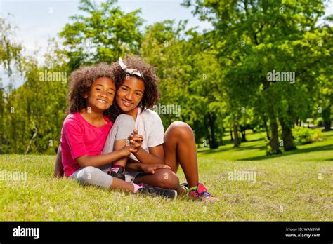Two Sisters Hold Hands Sitting In The Park Lawn Stock Photo Alamy