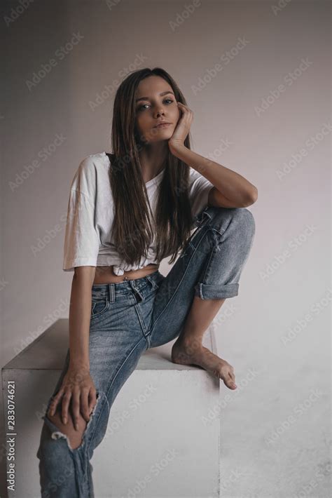 Sexy Hot Woman In Shirt Jeans And Sneakers Posing In Studio On Cube On White Background