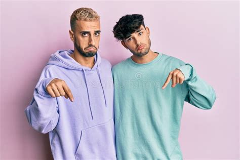 Homosexual Gay Couple Standing Together Wearing Casual Clothes Pointing Down Looking Sad And