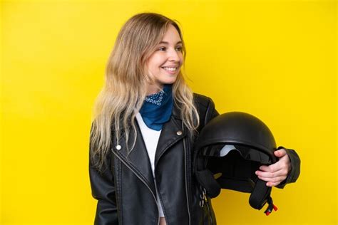 Blonde jeune fille anglaise avec un casque de moto isolé sur fond jaune à côté Photo Premium