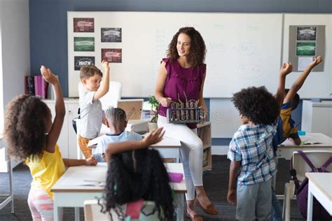 Multiracial Elementary Students Raising Hands While Caucasian Female