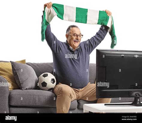 Mature Man Sitting On A Sofa Watching A Football Match And Cheering With A Scarf Isolated On