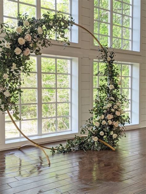 A Wedding Arch With Flowers And Greenery On The Floor In Front Of Two