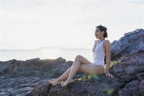 retrato de hermosa mujer de moda en bikini blanco posando en la playa de roca joven asiática