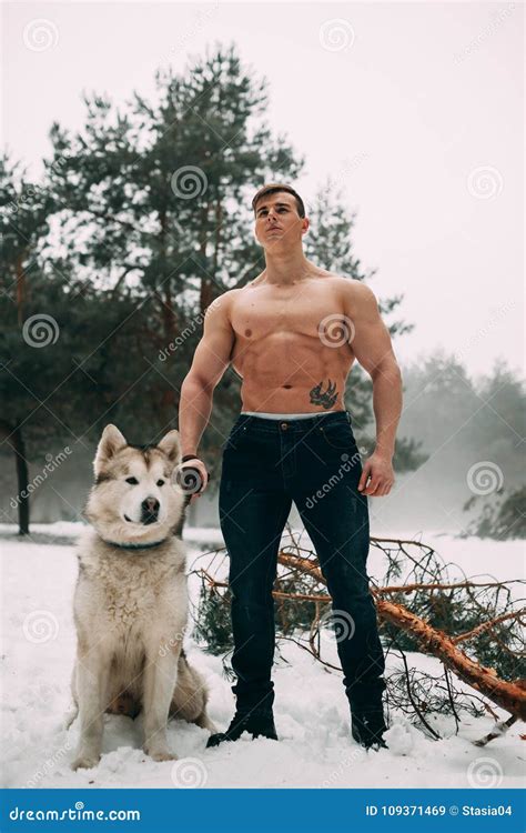 Young Bodybuilder With Bare Torso Leads Dog Malamute On Walk In Winter