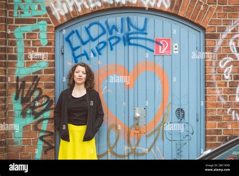Portrait Of Brunette Woman Standing In Front Of A Brick Wall With An Old Gate And Graffiti Stock