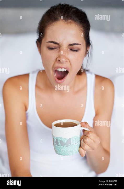 One Big Yawn A Young Woman Giving A Big Yawn While Sitting With A Cup