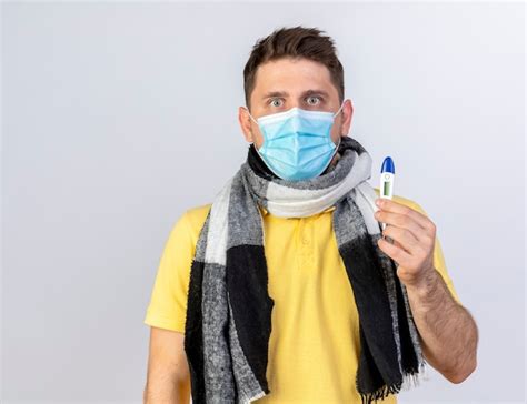 Choqué jeune homme slave malade blonde portant un masque médical et une écharpe détient un