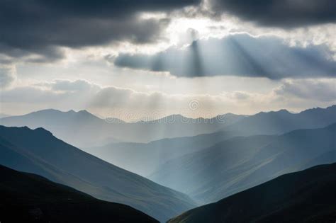 Serene Mountain Range With Misty Clouds And Rays Of Sunlight Peeking