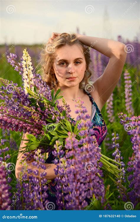 Une Fille Blonde De Charme Avec De Longs Cheveux Ondulés Pose Dans Un Domaine Avec Les Lupines