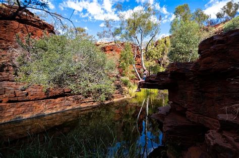 Ein Dschungelmädchen im Bikini sitzt auf Felsen an einem Bach in einer Schlucht im Karijini