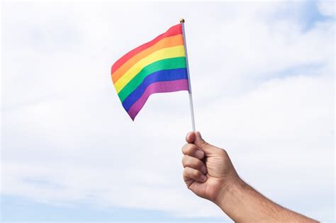 Hombre que sostiene la bandera del arco iris del símbolo del orgullo gay en el fondo del cielo