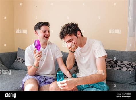 Latino Gay Couple Toasting And Laughing With Wine Glasses In Their Living Room Celebrating