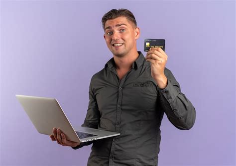 Jeune homme beau blonde surpris tient un ordinateur portable et une carte de crédit Photo Gratuite