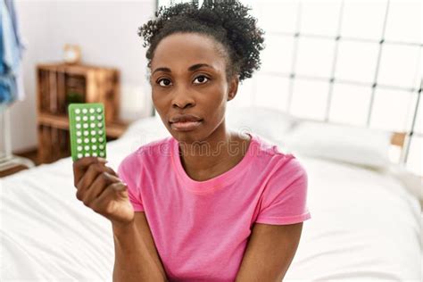 African American Woman Holding Birth Control Pills Sitting On Bed At